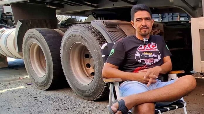 O motorista Leandro Barbosa sorrindo ao lado de seu caminhão, representando a rotina e a vida de caminhoneiro autônomo
