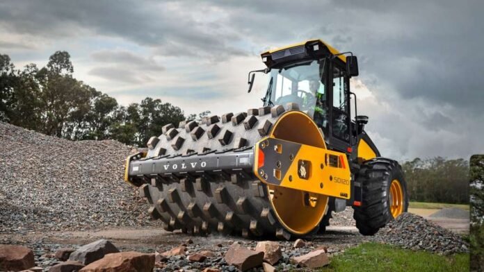 compactador Volvo SD120 amarelo operando em um canteiro de obras de infraestrutura, com foco no rolo compressor e na cabine
